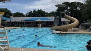 Una piscina con tobogán, rodeada de sillas de descanso y sombrillas.