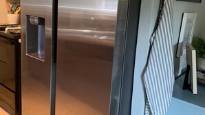 Un refrigerador de acero inoxidable en una cocina con piso de baldosas y un armario de madera.