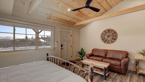 Une pièce spacieuse avec un grand lit, un canapé en cuir marron, une table basse en bois et une horloge en bois accrochée au mur.