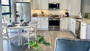 Une cuisine moderne avec des meubles blancs, des appareils en acier inoxydable et un coin repas comprenant des chaises blanches et une table dressée pour deux personnes.