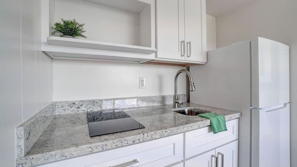 Eine Küche mit weißen Schränken, einer Granitarbeitsplatte, einem Spülbecken und einem Kühlschrank.