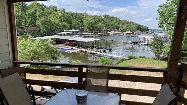 A covered outdoor seating area with a table and chairs, overlooking a lake with docks and boats. - Waterfront property perfect for a relaxing weekend or family get away (Osage Beach)