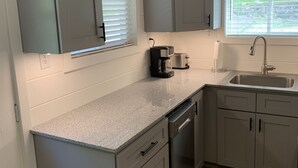 A modern kitchen with grey cabinetry, a granite countertop, a dishwasher, and a window with blinds. - Waterfront property perfect for a relaxing weekend or family get away (Osage Beach)