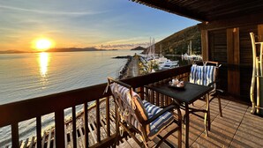 A wooden deck with a view of the sea and boats, a table with chairs, and a railing.