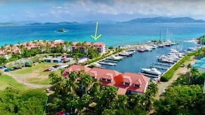A marina with multiple boats docked, surrounded by buildings with red roofs and palm trees.