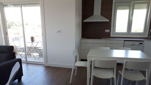 Una cocina moderna con armarios blancos, una mesa de comedor blanca con cuatro sillas y un amplio ventanal con persianas.