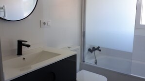 Un baño con espejo redondo, lavamanos, inodoro y ducha.