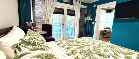 A hotel room with a bed, a chair, a table, and a view of the outside.