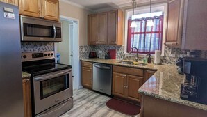 A kitchen with wooden cabinets, stainless steel appliances, a tiled backsplash, and a window with curtains.