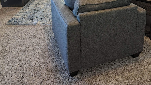 A living room with a large grey sofa, a smaller grey sofa, a coffee table, a TV, a Christmas tree, and a window with blinds.
