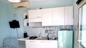 Een kleine keuken met witte kastjes, een gasfornuis, een spoelbak en een koelkast.