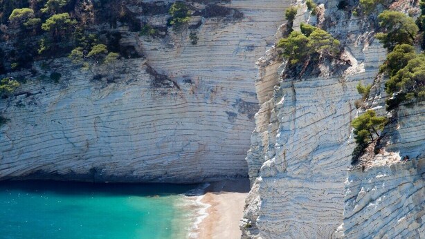 Een klif aan de kust met een smal strand en turkoois water.