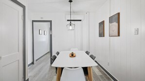 Ett modernt matområde med ett vitt bord, svarta stolar och en hängande lampa.