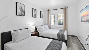 Ett hotellrum med två sängar, ett fönster med gardiner, en tavla på väggen och en taklampa.