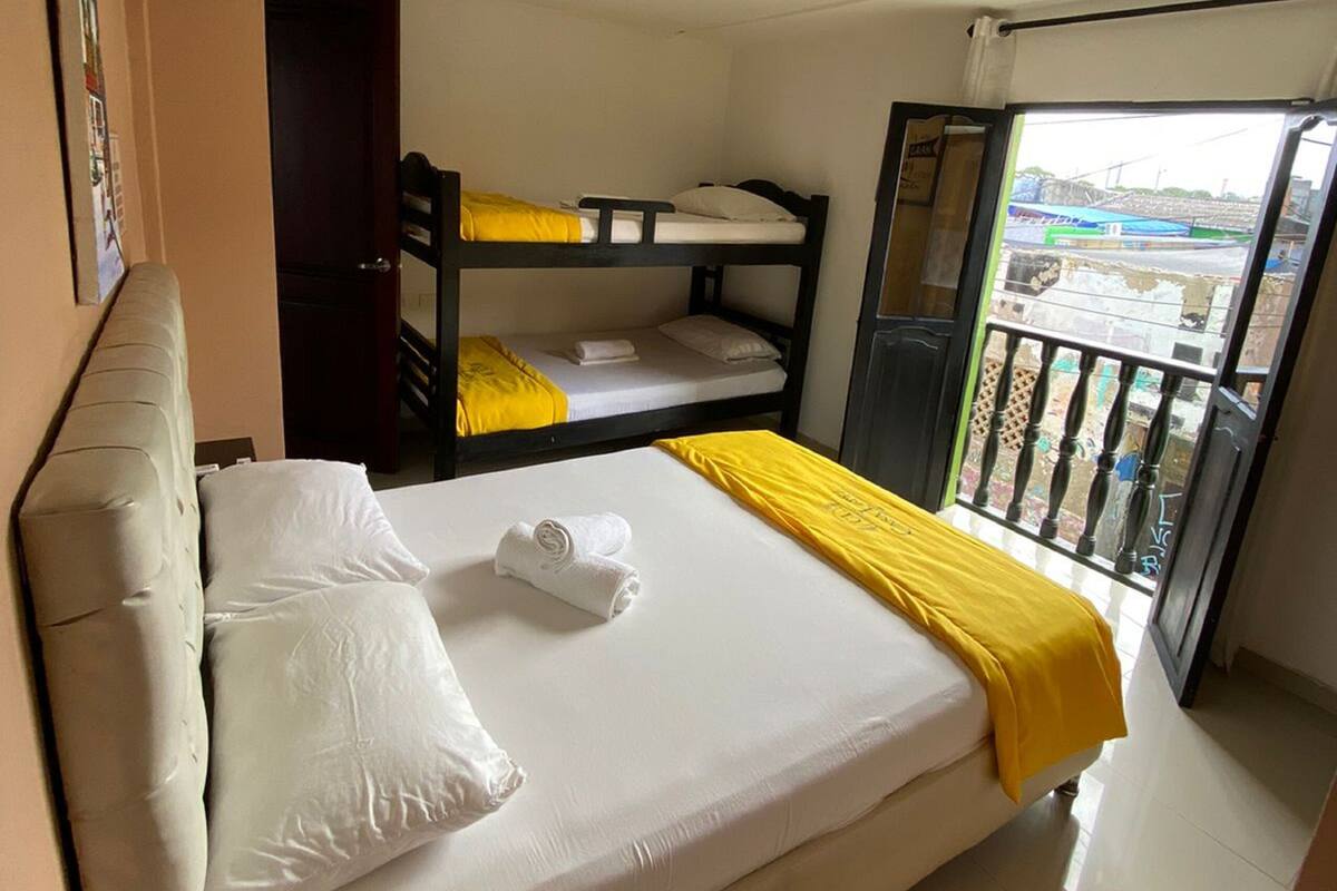 Una habitación de hotel con una cama grande, una cama nido más pequeña, un balcón con vistas y una puerta que da a un balcón.