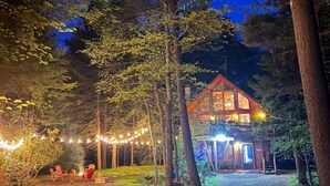 A two-story wooden cabin with a porch, surrounded by trees and string lights.