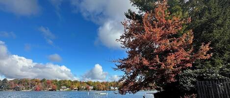 Blick auf einen See mit einem hölzernen Steg, der sich ins Wasser erstreckt, umgeben von herbstlich gefärbten Bäumen und einem klaren Himmel.