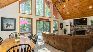 A spacious living area with a wooden ceiling, large windows, a stone fireplace, and a cozy seating arrangement.