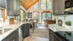 A modern kitchen with dark cabinets, a wooden ceiling, and large windows.