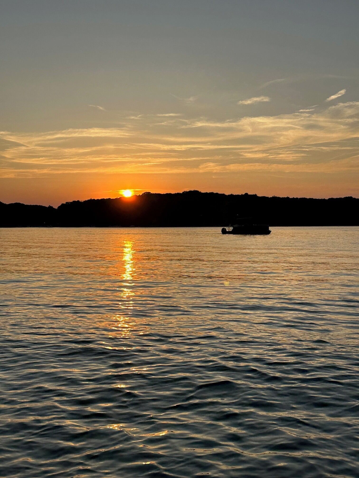 Un coucher de soleil sur une étendue d’eau calme, avec un bateau visible au loin.