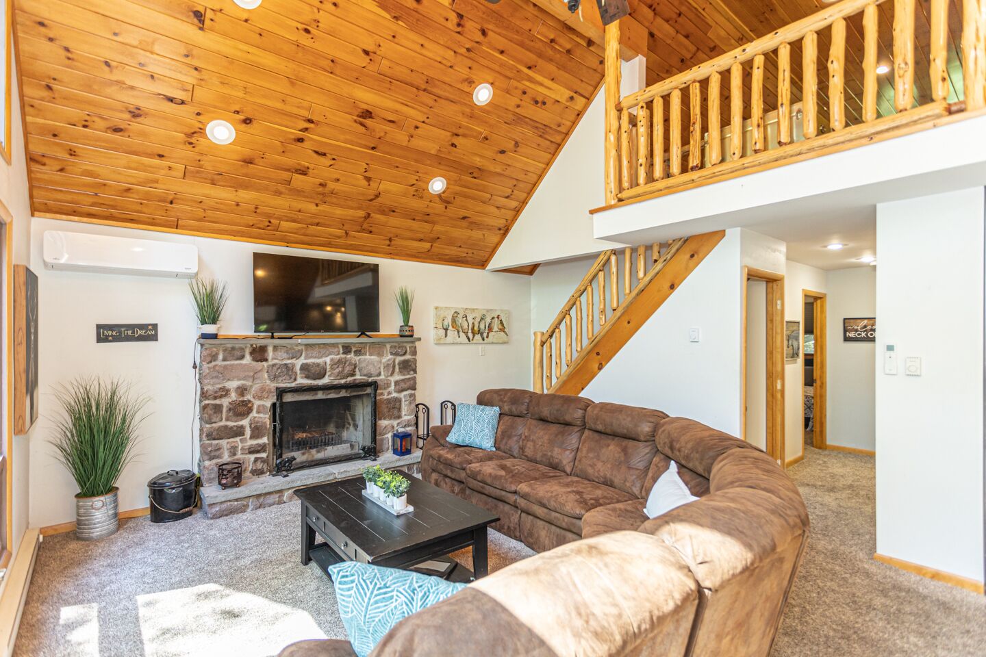A cozy living room with a stone fireplace, a large brown leather sofa, and a wooden ceiling.