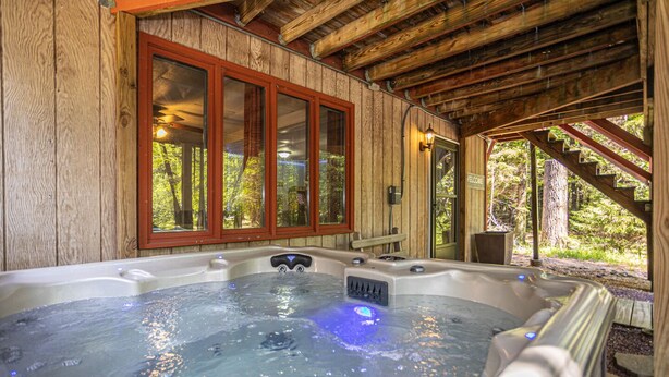 A wooden cabin with a hot tub and a staircase leading to a deck.