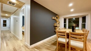 Un comedor con mesa y sillas de madera, una pared de acento negra y vistas al exterior a través de una ventana.