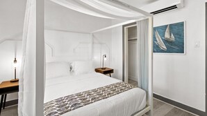 Een slaapkamer met hemelbed, nachtkastje met lamp, en een schilderij van zeilboten aan de muur, plus een airconditioner.