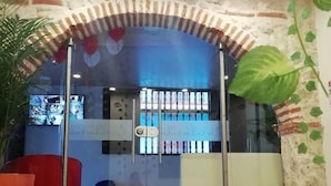 A reception area with a glass door, a red chair, a large potted plant, and a patterned floor. - CL-11 Habitación en Getsemaní con wifi (Cartagena)