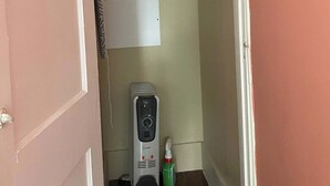A small, narrow room with a bed at the top, a whiteboard on the wall, and a cleaning device on the floor.
