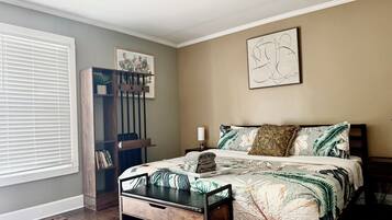 Um quarto com uma cama, mesa de cabeceira, estante, janela com persianas e ventilador de teto.