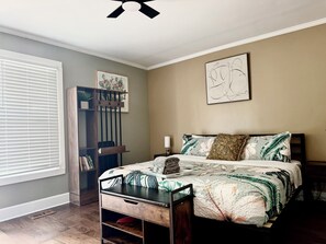 A bedroom with a bed, a nightstand, a bookshelf, a window with blinds, and a ceiling fan.
