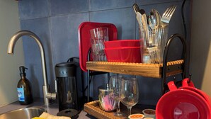 A kitchen with a stainless steel sink, a coffee maker, a red dish rack, and a tray with cups and a wine glass.