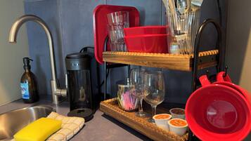 A kitchen with a stainless steel sink, a coffee maker, a red dish rack, and a tray with cups and a wine glass.