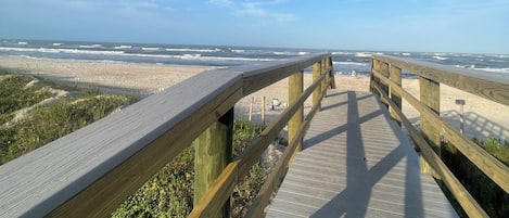 Une promenade en bois qui mène à une plage, d’où l’on a une vue dégagée sur l’océan et le lointain rivage.