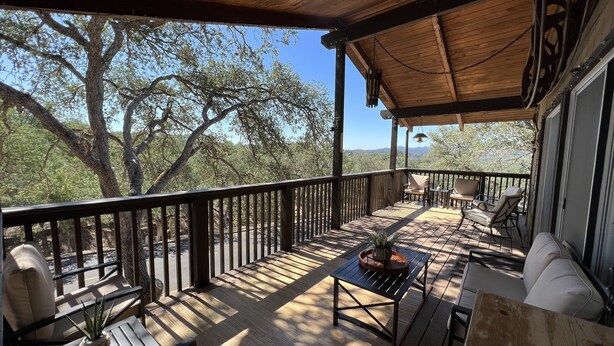 A wooden deck with outdoor furniture, including chairs and a table, overlooking a mountainous landscape.