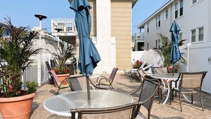 An outdoor patio with round tables and wicker chairs, surrounded by potted plants and umbrellas.