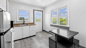 A modern kitchen with white cabinets, a stainless steel refrigerator, a dark countertop, and two windows providing views of greenery.