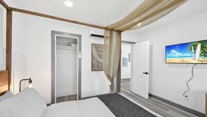 A hotel room with a bed, a television mounted on the wall, and a door leading to another room.