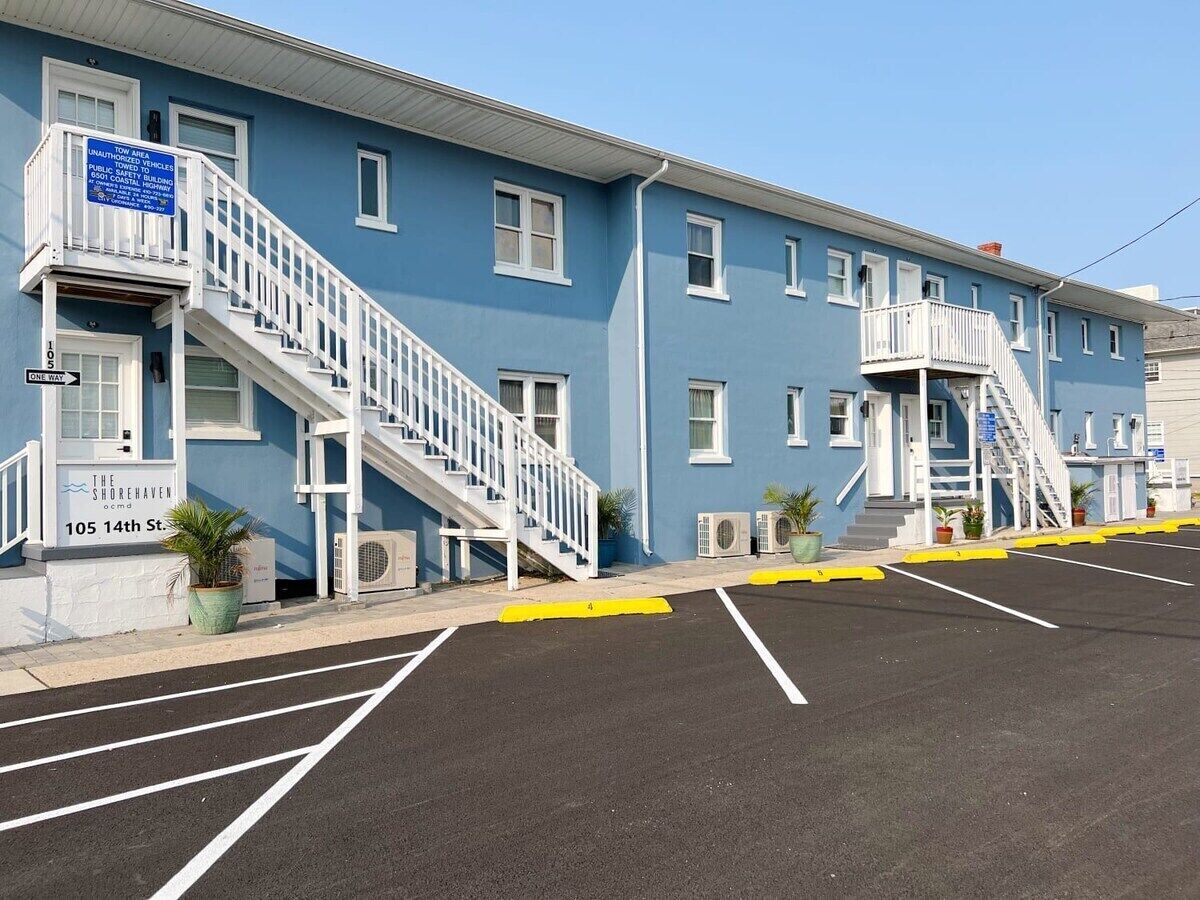 A blue building with a staircase leading to the entrance, a parking lot with marked spaces, and a sign indicating it's a public building.