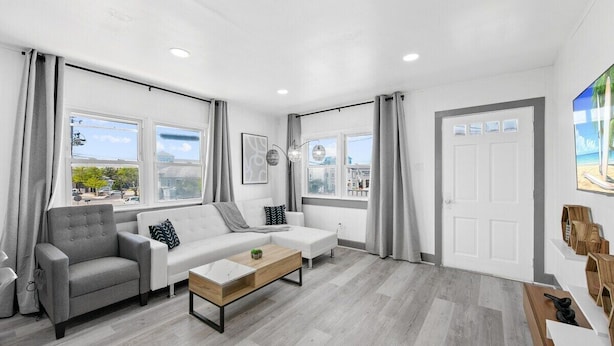 A modern living room with a grey sofa, a white sofa, a wooden coffee table, and a view of the city through large windows.