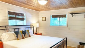 A bedroom with a bed, nightstands, a bench, and windows with blinds.