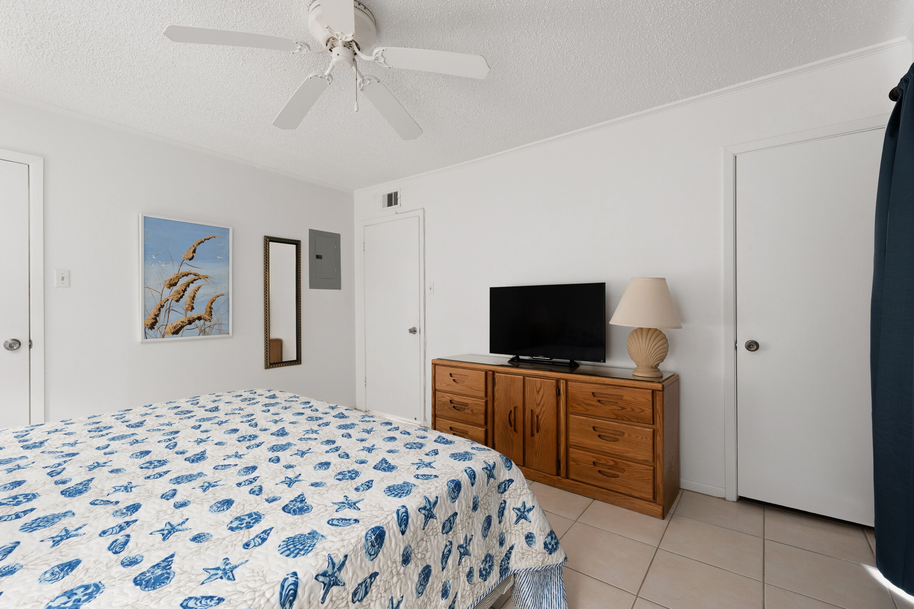 Un dormitorio con una cama, un televisor sobre un mueble de madera, un ventilador de techo y una puerta.
