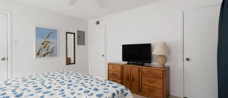 Un dormitorio con una cama, un televisor sobre un mueble de madera, un ventilador de techo y una puerta.