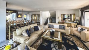 En rummelig stue med en stor sofa, et sofabord og et spiseområde med stole og en lysekrone.