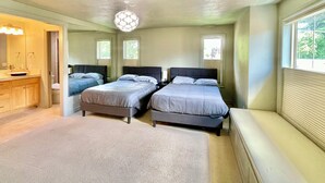 A bedroom with two beds, a vanity with a mirror, and a window with blinds.