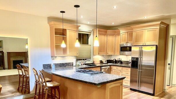 A modern kitchen with wooden cabinets, a stainless steel refrigerator, and a granite countertop.