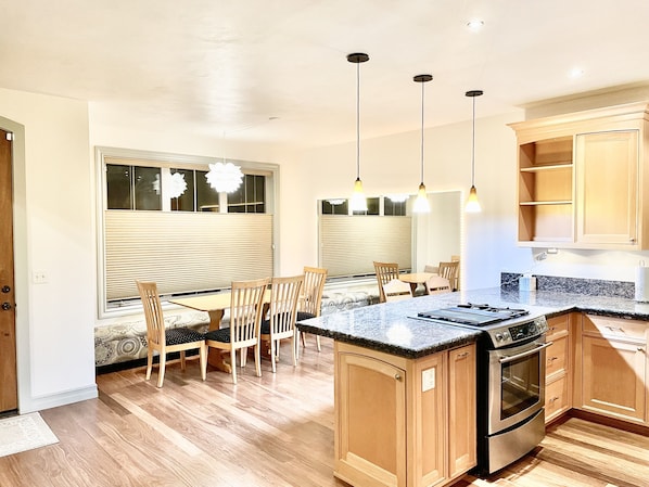 Une cuisine dotée de meubles en bois, d’un plan de travail en granit, d’un four encastré et de luminaires suspendus.