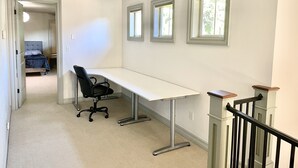 A bedroom with a bed, a desk, and a chair. There are three windows on the wall.