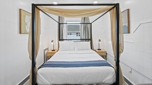 A modern bedroom with a canopy bed, bedside lamps, and artwork on the walls.